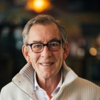 Jim Kern, a respectable-looking gentlemen in glasses and a white sweater, smiles at the camera.